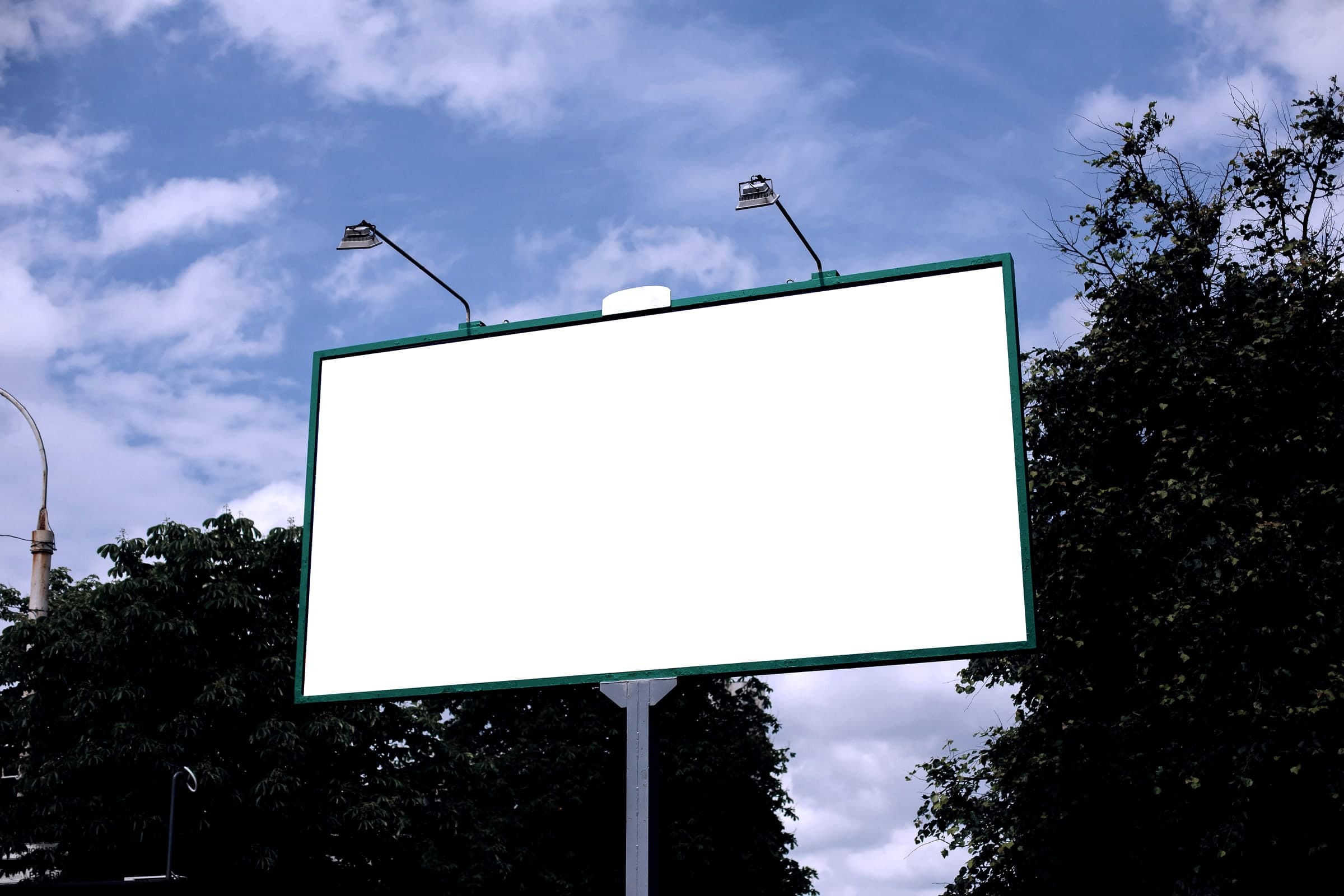 Beleuchtete Plakatwand mit Strahlern, umgeben von Bäumen